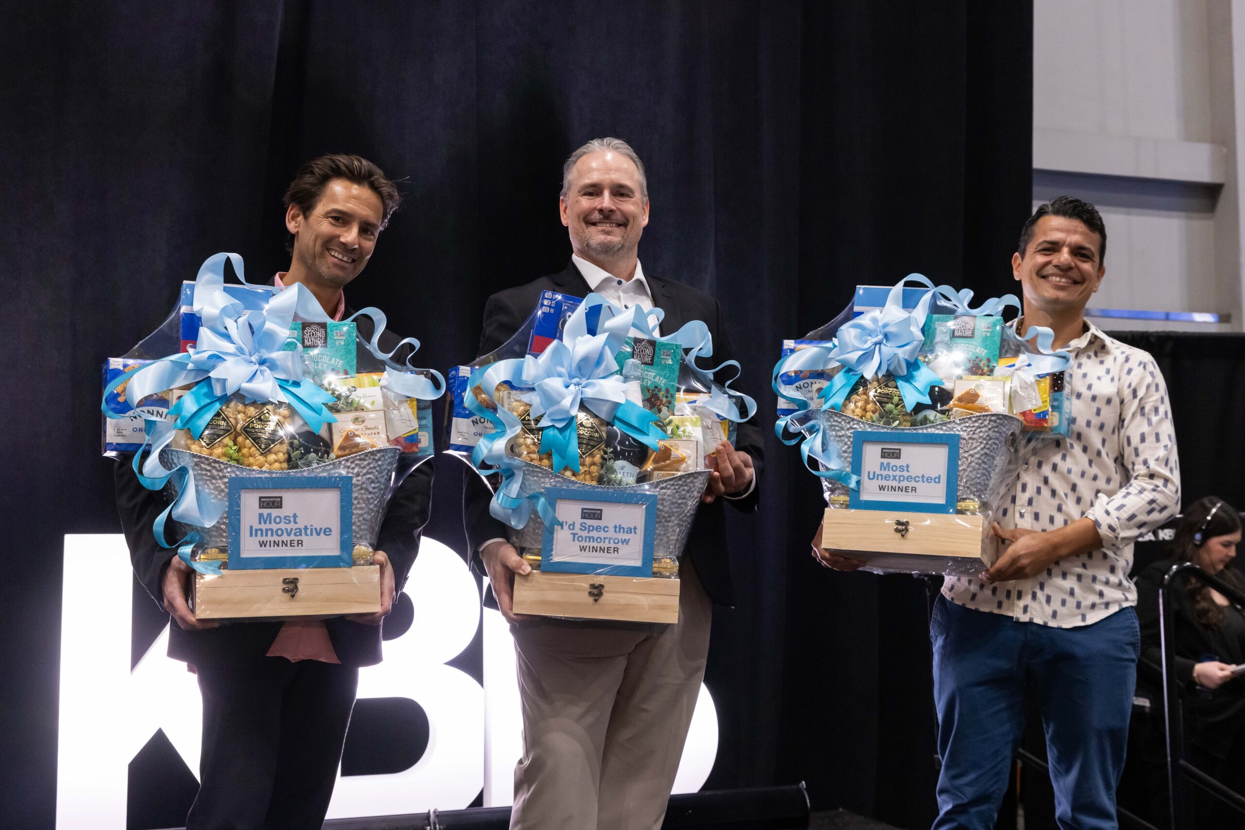 A panel with three designers sitting in chairs in front of a large projection screen takes place at KBIS 2024 on NEXTStage. 