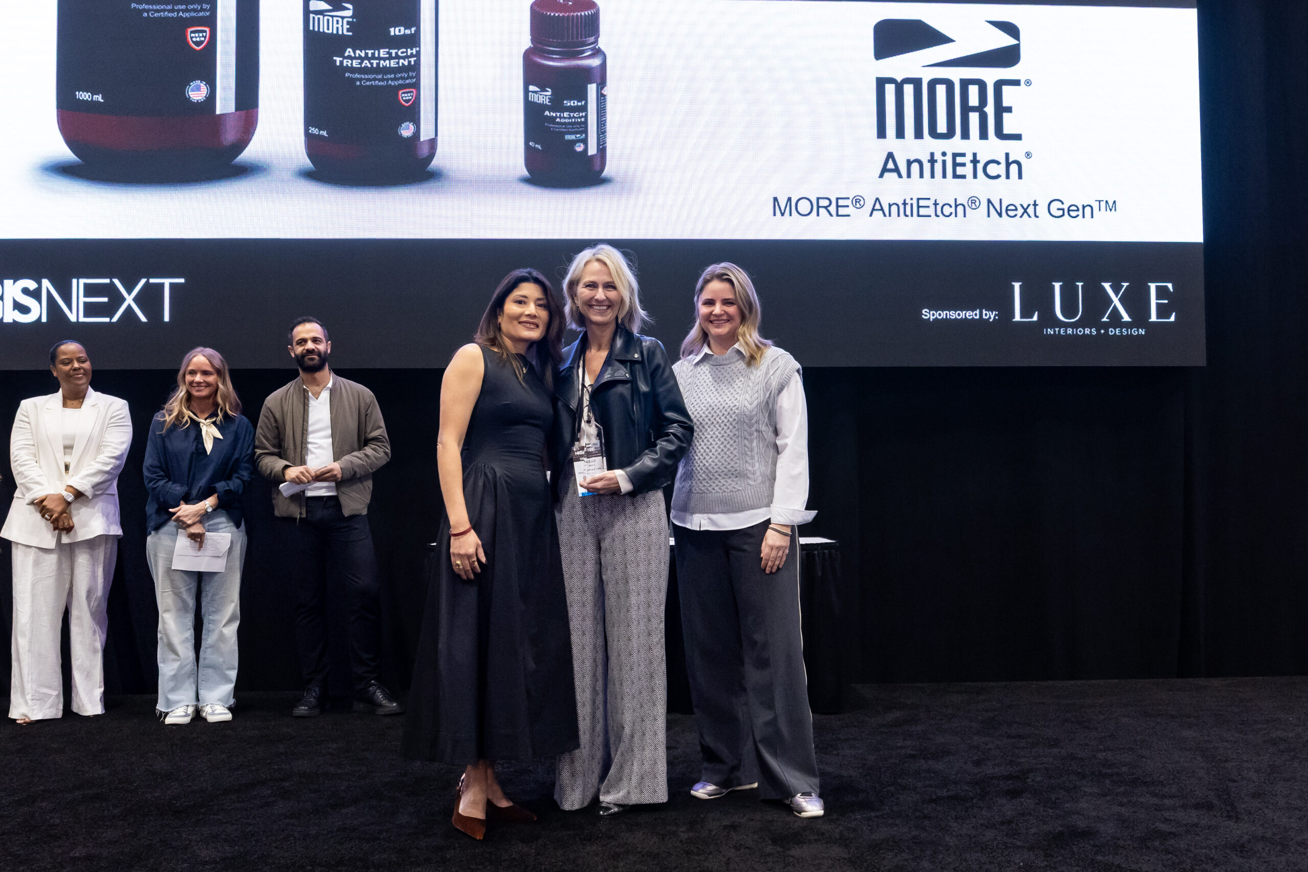 A man waves hello in the middle of a crowd at KBIS 2024 in a hall lined with purple carpet.